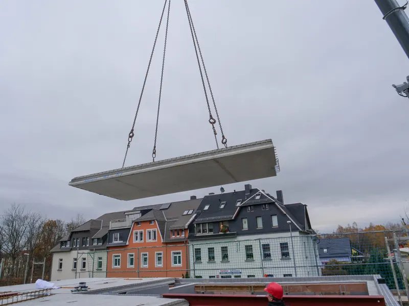 Ein Deckenelement schwebt am Kran über der Baustelle ein