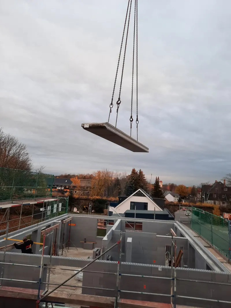 Ein Deckenelement hängt am Kran über dem Rohbau