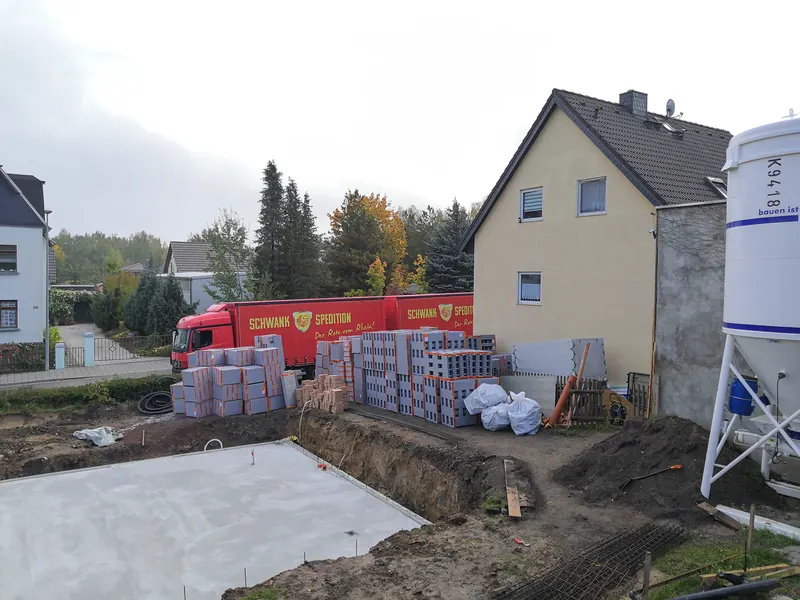Gelieferter Hausbausatz auf der Baustelle neben der fertigen Bodenplatte