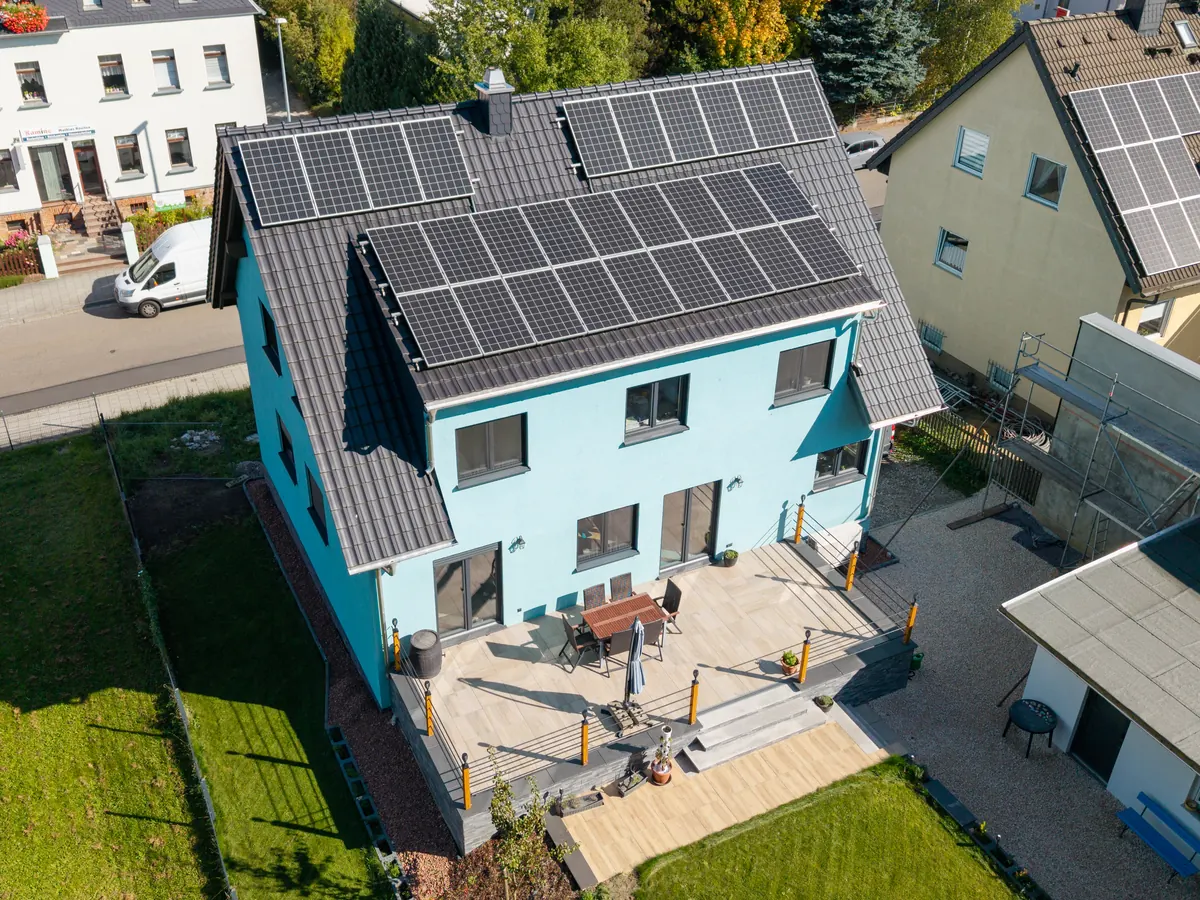 Luftbild des hellblauen isorast-Wohnhauses mit Photovoltaik auf dem Satteldach, Terrasse und Garten