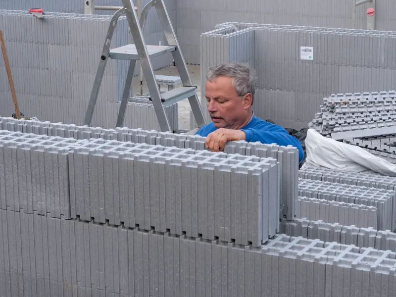 Ein Elementstein wird von Hand auf die bereits gestellte Wand gesteckt