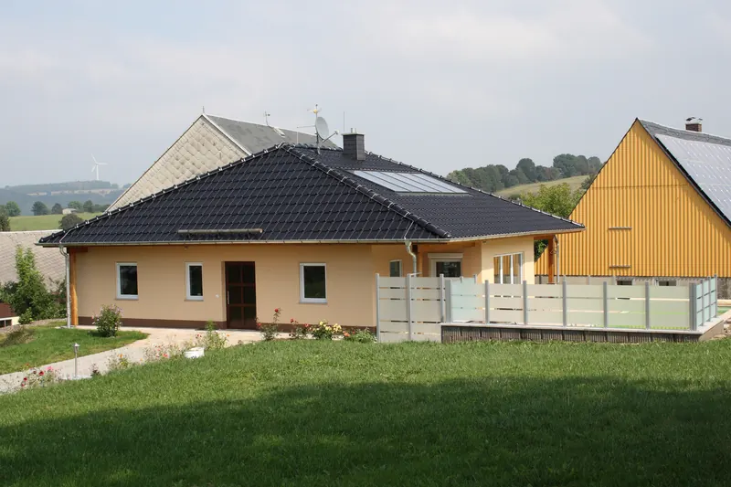 Bungalow mit Walmdach und Garten, im Vordergrund die Poolumrandung