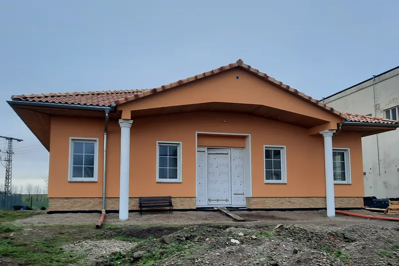 Apricotfarbener Bungalow mit Walmdach aus Tonziegeln, Giebelvorbau auf weißen Säulen über dem Eingang und Natursteinsockel