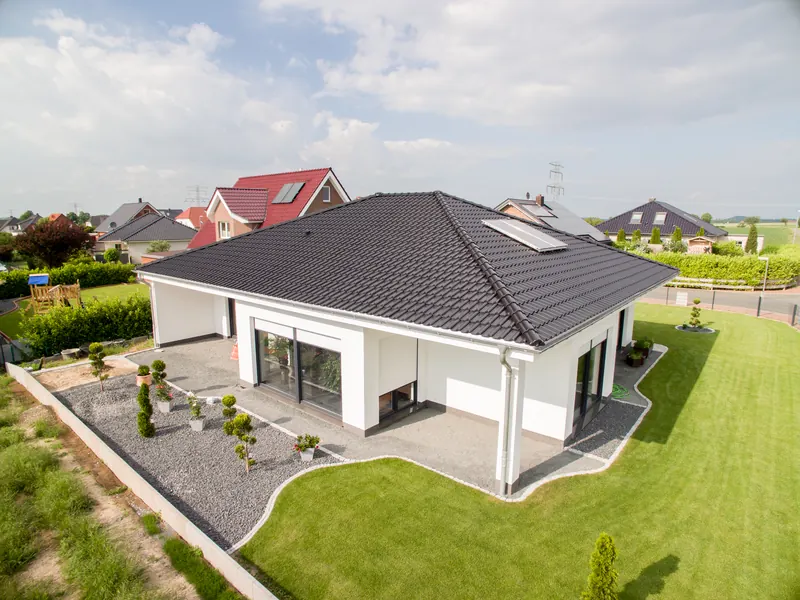 Weißer Bungalow mit dunklem Walmdach, großen Glasflächen und angelegtem Garten
