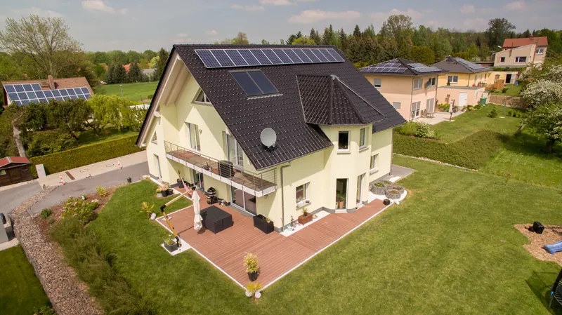 Luftbild: helles Einfamilienhaus mit Erkerturm, Photovoltaik und großer Holzterrasse