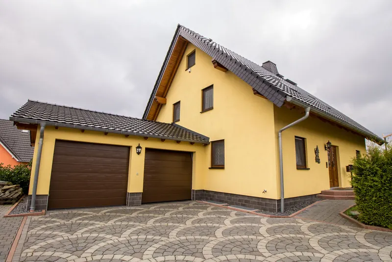 Gelbes Einfamilienhaus mit Doppelgarage und gepflasterter Einfahrt