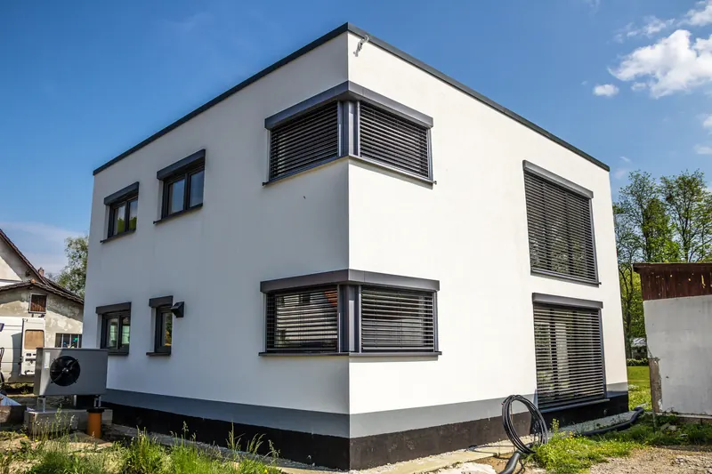 Weißes, kubisches Haus mit Flachdach und dunklen Fensterrahmen