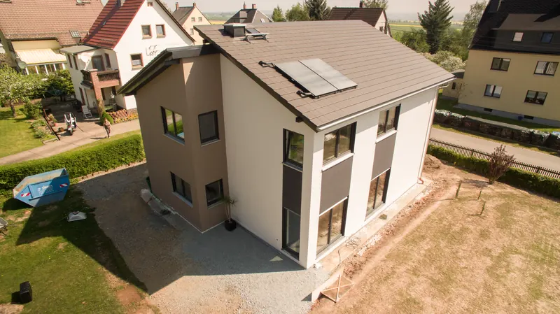 Luftbild: zweifarbiges Einfamilienhaus mit Satteldach und Solarkollektoren kurz nach Fertigstellung