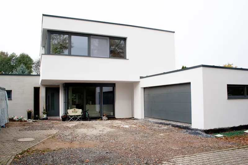 Weißes Flachdachhaus mit auskragendem Obergeschoss über dem verglasten Eingang und angebauter Garage