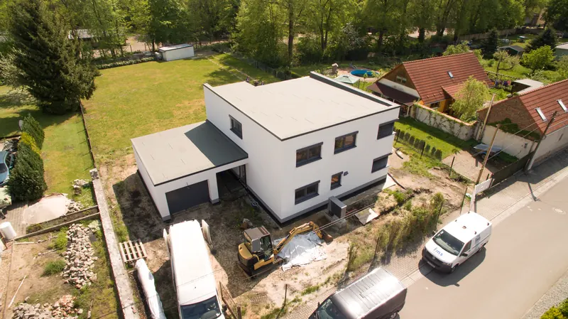 Luftbild: weißes, zweigeschossiges Flachdachhaus mit angebauter Garage während der Außenarbeiten