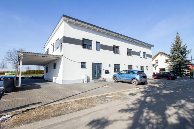 Langes, weißes Mehrfamilienhaus mit Satteldach und Carport