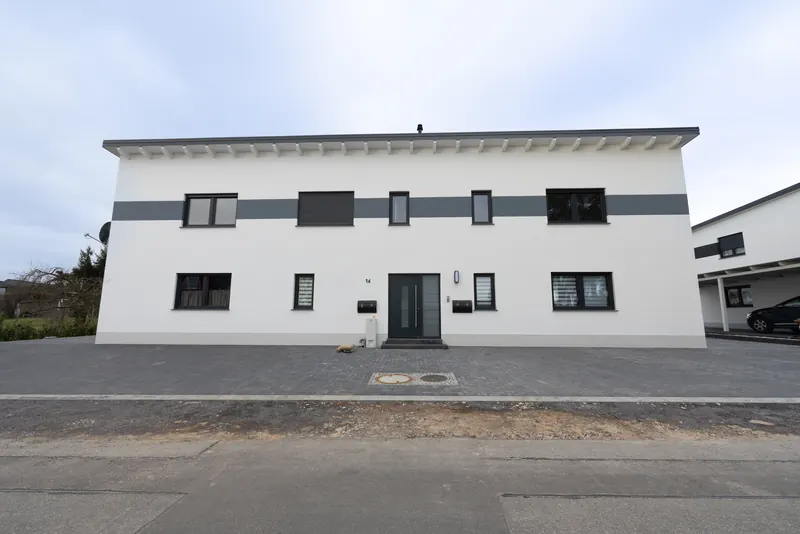 Zweigeschossiges, weißes Mehrfamilienhaus mit Pultdach und grauem Fassadenband