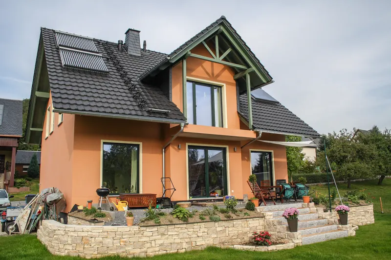 Passivhaus mit orangefarbener Fassade, Holzgiebel und Terrasse
