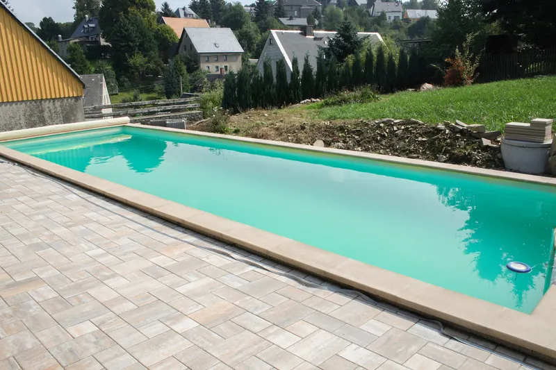 Schwimmbecken mit türkisfarbenem Wasser und gepflasterter Umrandung im Garten