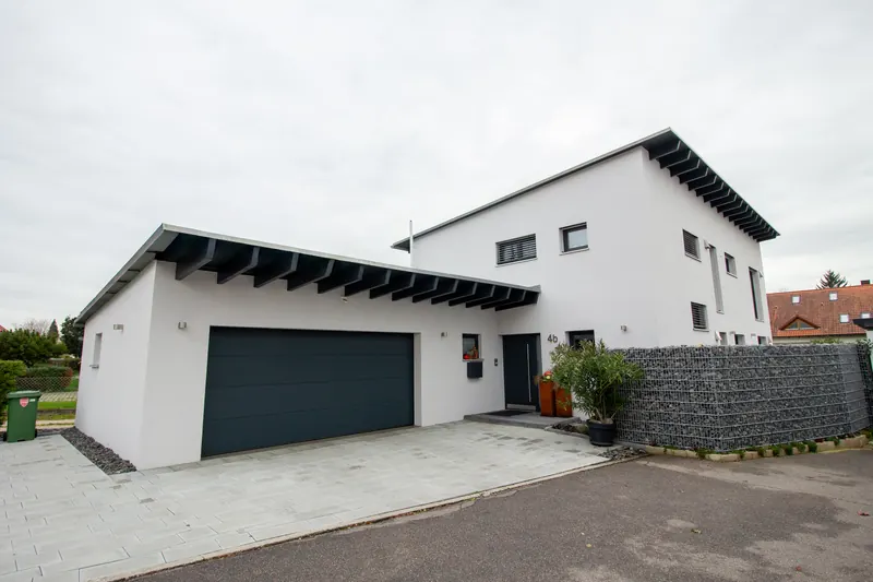 Weißes Einfamilienhaus mit Pultdach, sichtbaren Sparren im Dachüberstand und angebauter Doppelgarage mit Pultdach
