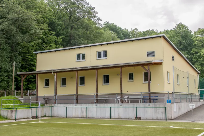 Zweigeschossiges Sozialgebäude mit überdachter Veranda an einem Sportplatz